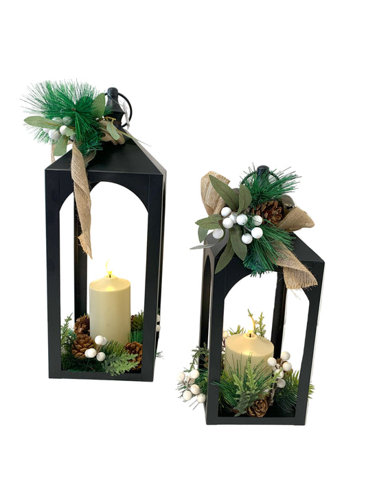 Two black lanterns with candles and decorative greenery on a white background